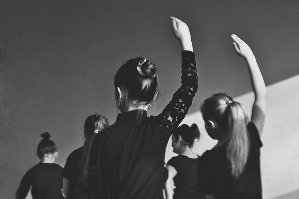 Grayscale image of multiple ballerinas captured in mid-dance, viewed from behind.